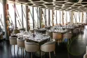 Modern panoramic restaurant interior with contemporary seating, tables set for dining, floor-to-ceiling windows overlooking Bordeaux cityscape, geometric ceiling design, and neutral-toned furnishings.
