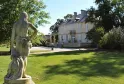 Stone statue of a female figure in the gardens of Château Kirwan in Bordeaux, with the 18th-century mansion visible in the background surrounded by trees
