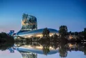 Night view of the Cité du Vin museum in Bordeaux, an illuminated modern building with curved glass and steel architecture reflected in the adjacent river.