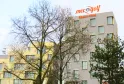 Exterior view of Mer & Golf Aparthotel, a modern multi-story building with beige and yellow facades, featuring regular window arrangements and the hotel signage on top, surrounded by bare trees in winter.