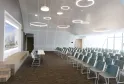 Modern conference room at Hilton Garden Inn Bordeaux Centre with rows of gray chairs, a presentation screen displaying an architectural project, wooden bench seating, and circular pendant lighting fixtures on the ceiling.