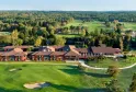 Aerial view of a luxury red-brick golf resort with modern architecture, featuring manicured greens, bunkers, and a clubhouse overlooking a river and forested landscape.